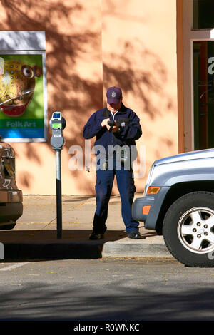 A male parking enforcement officer digitally writes a ticket for a vehicle whose parking time has elaspsed in downtown Santa Fe NM, USA Stock Photo