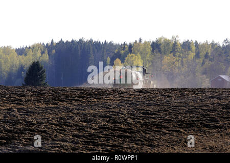 Salo, Finland - May 11, 2018: Farmer spreading manure on tilled field with tractor and spreader on a beautiful spring evening in South of Finland. Stock Photo