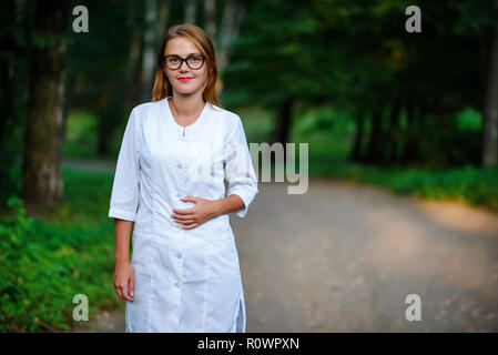 a young girl who is a doctor stands outside, holds the left hand on the belly. Stock Photo