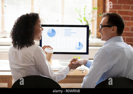 Diverse employees handshake working together at pc in office Stock Photo
