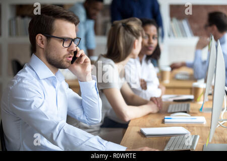 Serious male employee talk on phone working at computer Stock Photo