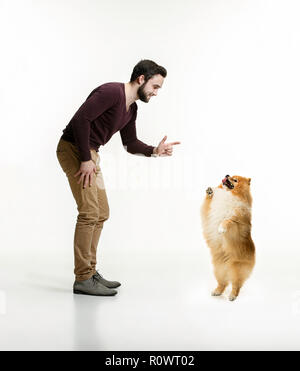Emotional Portrait of man and his dog, concept of friendship and care of man and animal. The cute Little young pomeranian cob isolated over white studio background Stock Photo