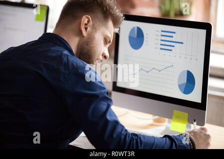 Male employee working with graphs on pc in office Stock Photo