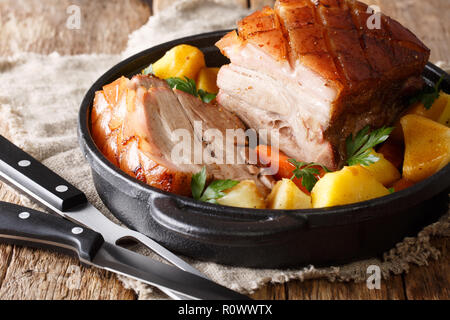 Tasty crispy pork baked in beer with vegetables and gravy close-up in a frying pan on the table. horizontal Stock Photo