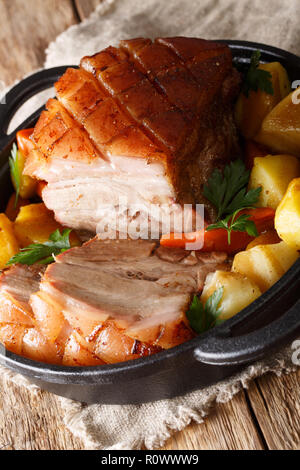 Krustenbraten Pork Roast with Crispy Rind with vegetables close-up in a frying pan on the table. Vertical