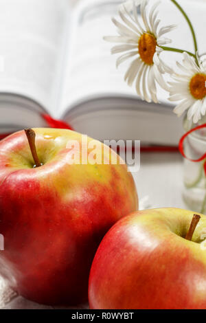 Two big red apples with opened book and chamomiles on the background Stock Photo