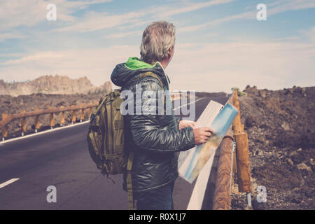 portrait of adventure senior man with map and extreme explorer gear on mountain with long straight road in front of him for a long walk. wanderlust an Stock Photo