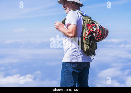 Old man traveler portrait enjoy the clouds view on the top - backpack and colored retro style blanket on the back. Happy lifestyle and modern people - Stock Photo
