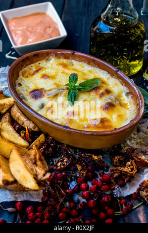 Meat baked in cheese on a wooden table decorated with potatoes herbs and spices Stock Photo