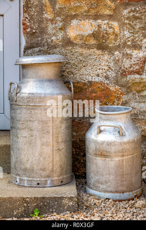 Two traditional milk churns on a door step, agsinst a stone wall. Stock Photo