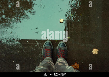 Standing in the drizzle puddle on the street, top view of sneakers in water Stock Photo