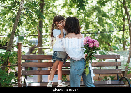 Young mother and daughter on bench with a bouquet of pink peonies Stock Photo