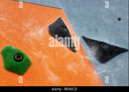 Two black and one green crimper rock climbing holds against an orange and grey wall Stock Photo