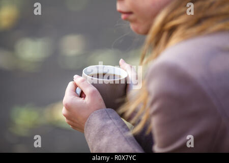 Close up of woman drinking from a cup against autumn leaves pattern Stock Photo