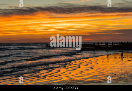 Evening sky after sunset with orange and red sky reflecting in sand ridges by the sea in West Sussex, UK. Stock Photo