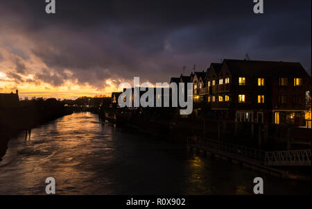 Sun setting over the River Arun on a cloudy Autumn evening with fiery sunset in the sky in Arundel, West Sussex, England, UK. Riverside housing. Stock Photo