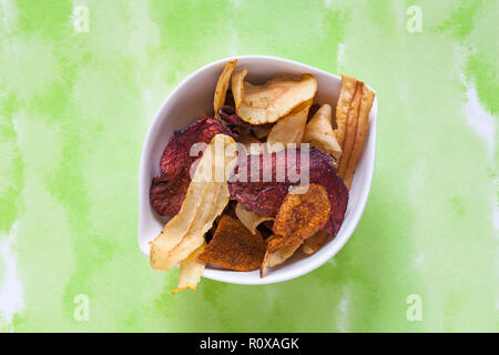 Bowl of Tyrrells veg crisps hand-cooked English crisps isolated on green patterned background - parsnip, beetroot & carrot crisps with sea salt Stock Photo