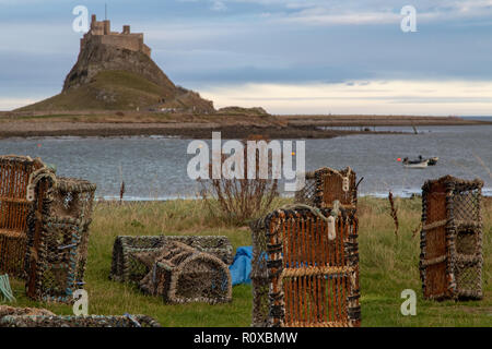 A view of Lindisfarne castle on a sunny and cloudy day. In the foreground are lobster pots and other fishing gear. Stock Photo