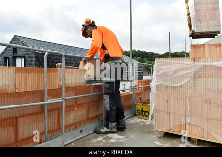 a construction worker building a wall with large orange-red clay blocks on an outdoor job site - France Stock Photo