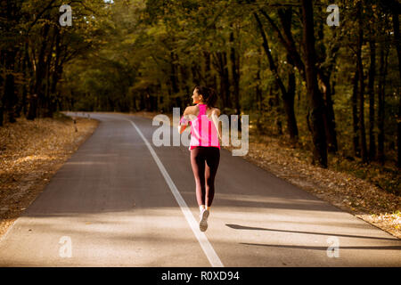 Young fitness woman running at forest trail in golden autumn Stock Photo