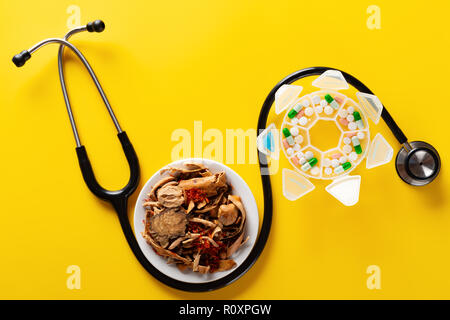 studio shoot Chinese herb medicine and pills wrapped with a stethoscope on yellow background Stock Photo