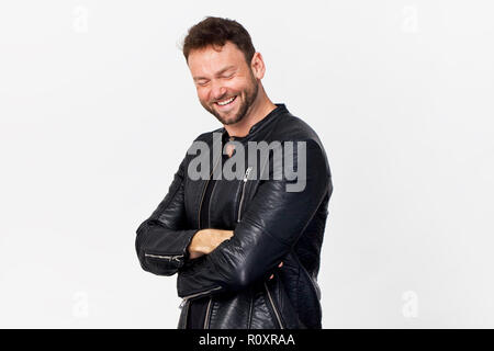 Smiling positive male with attractive look, wearing black jacket, posing against white blank wall Stock Photo