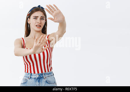 Stop taking my photos. Portrait of annoyed silly and timid insecure attractive woman in striped pinup top and headband pulling palms forward to protect face from camera being displeased and irritated Stock Photo