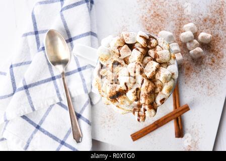 Overhead view of a mug of hot chocolate with toasted marshmallows sprinkled with cinnamon. A spoon towel and cinnamon sticks Stock Photo