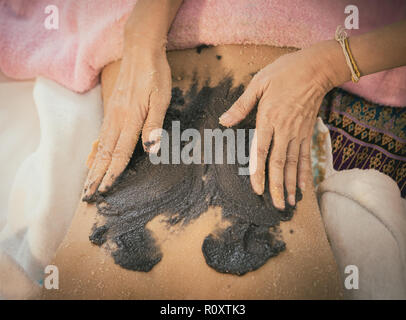 Spa Therapist is applying Charcoal coffee scrub on to a woman back Stock Photo