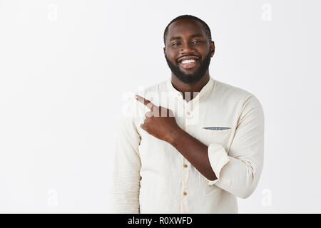 Proud and satisfied handsome African-american businessman pointing left as showing chart being delighted and happy present project of team smiling broadly at camera as posing over gray background Stock Photo