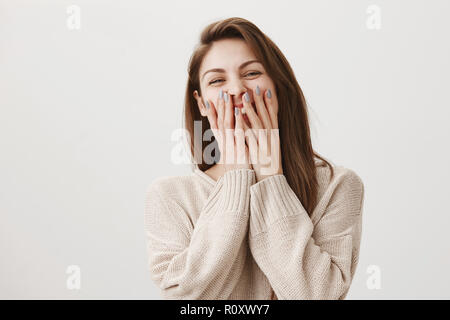 Attractive nail master laughs with her coworkers while there is no clients. Portrait of emotive gorgeous female covering mouth with both hands while laughing out loud, hearing hilarious joke Stock Photo