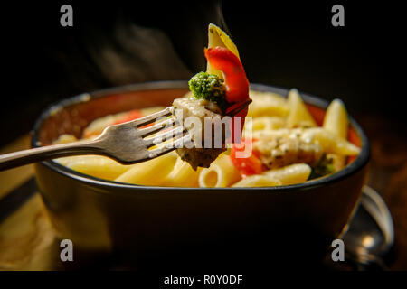Grilled chicken alfredo penne primavera with dark moody lighting on rustic wooden kitchen table Stock Photo