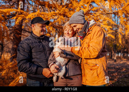Happy family spending time with pug dog in autumn park. Parents with their son hugging pet. Family values Stock Photo