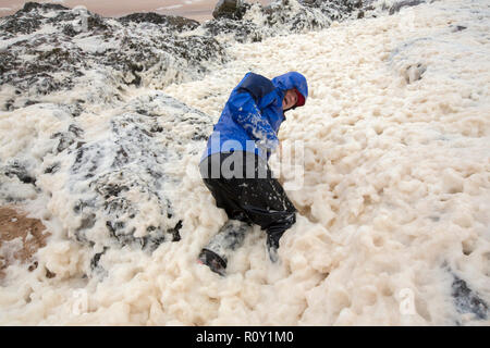 A hiker playing in spume or sea foam on the beach at Sandwood Bay during gale force winds, Sutherland, Scotland, UK. Stock Photo