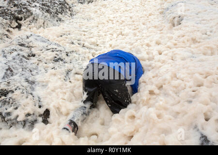 A hiker playing in spume or sea foam on the beach at Sandwood Bay during gale force winds, Sutherland, Scotland, UK. Stock Photo