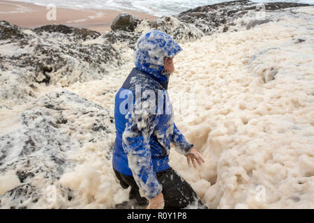 A hiker playing in spume or sea foam on the beach at Sandwood Bay during gale force winds, Sutherland, Scotland, UK. Stock Photo