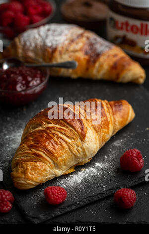 Croissants with icing sugar surrounded with raspberries, raspberry jam and nutella Stock Photo
