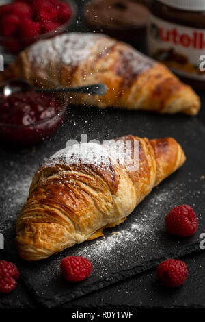 Croissants being dusted with icing sugar surrounded with raspberries, raspberry jam and nutella Stock Photo