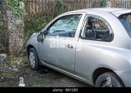 Dumped on the street a stolen car is left vandalised and broken with smashed glass and the wing mirror hanging off. Stock Photo