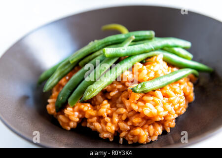 Macro closeup side view of risotto Italian arborio cooked rice with tomato sauce, olive oil, green beans on top in brown dish, plate on table Stock Photo