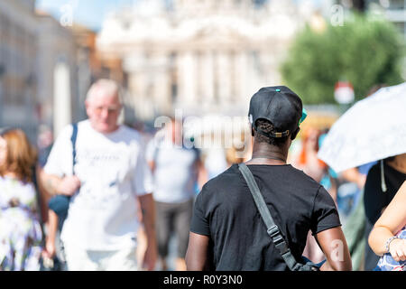 Rome, Italy - September 5, 2018: African black male, man, immigrant walking on street, road with many Italian people, Vatican city, St Peters Basilica Stock Photo