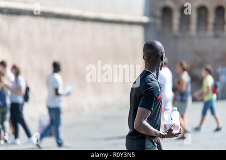 Rome, Italy - September 5, 2018: African black male, man, immigrant, street vendor, seller selling bottled bottles of water, walking road sidewalk wit Stock Photo