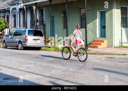 New Orleans, USA - April 22, 2018: Street in Louisiana town, city, woman on bicycle bike riding by building during sunny day Stock Photo