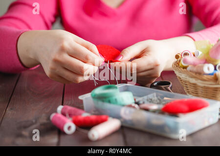 Woman sews red heart shaped toy by needle, conceptual symbol of love Stock Photo