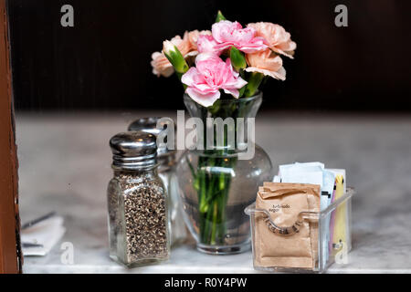 Closeup of salt, pepper and brown raw turbinado sugar shakers, packets, bottles on marble granite table, window in cafe restaurant, flowers in vase Stock Photo