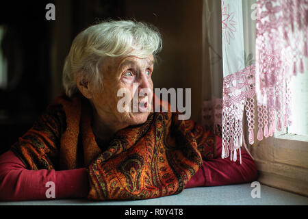 Portrait of elderly woman sitting in the house looks out the window. Stock Photo