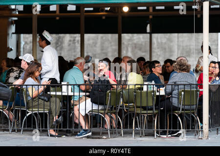 New Orleans, USA - April 22, 2018: People sitting at tables at famous, iconic Cafe Du Monde shop, restaurant famous for beignet powdered sugar donuts,
