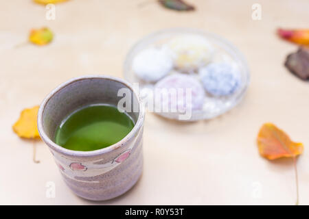 Green tea cup and mochi rice cake Japanese dessert wagashi, colorful daifuku, autumn season leaves on table, vibrant color Stock Photo