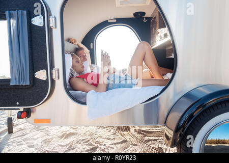 Woman lying in trailer near her boyfriend using smartphone reading messages Stock Photo