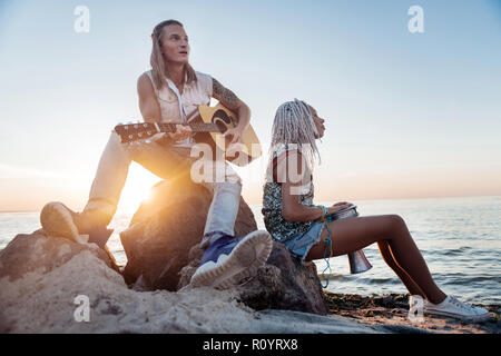 Blonde-haired man with tattoo on hand playing the guitar near his woman Stock Photo